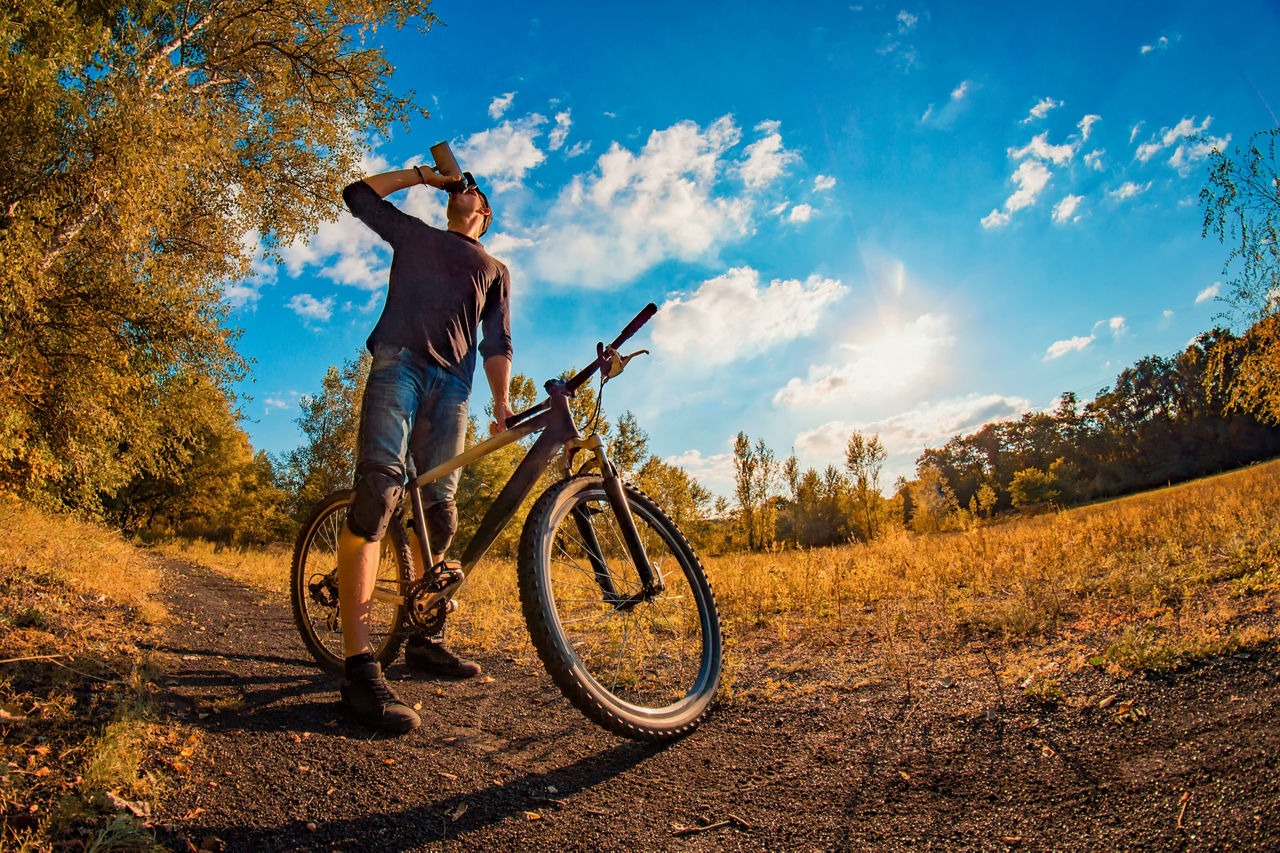 Young man drinks a protein shake from a shaker while taking a bike ride in the fall season