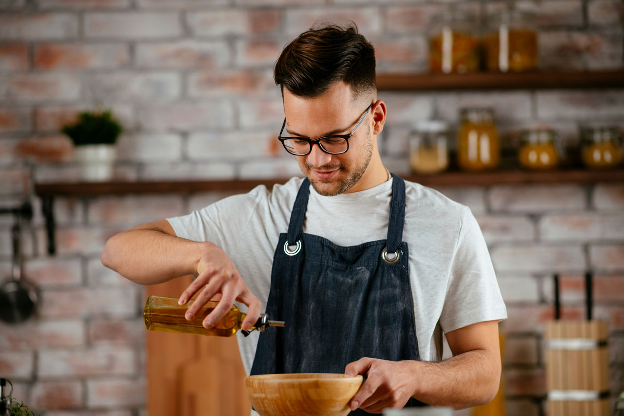 Young man making a meal in his kitchen using oil